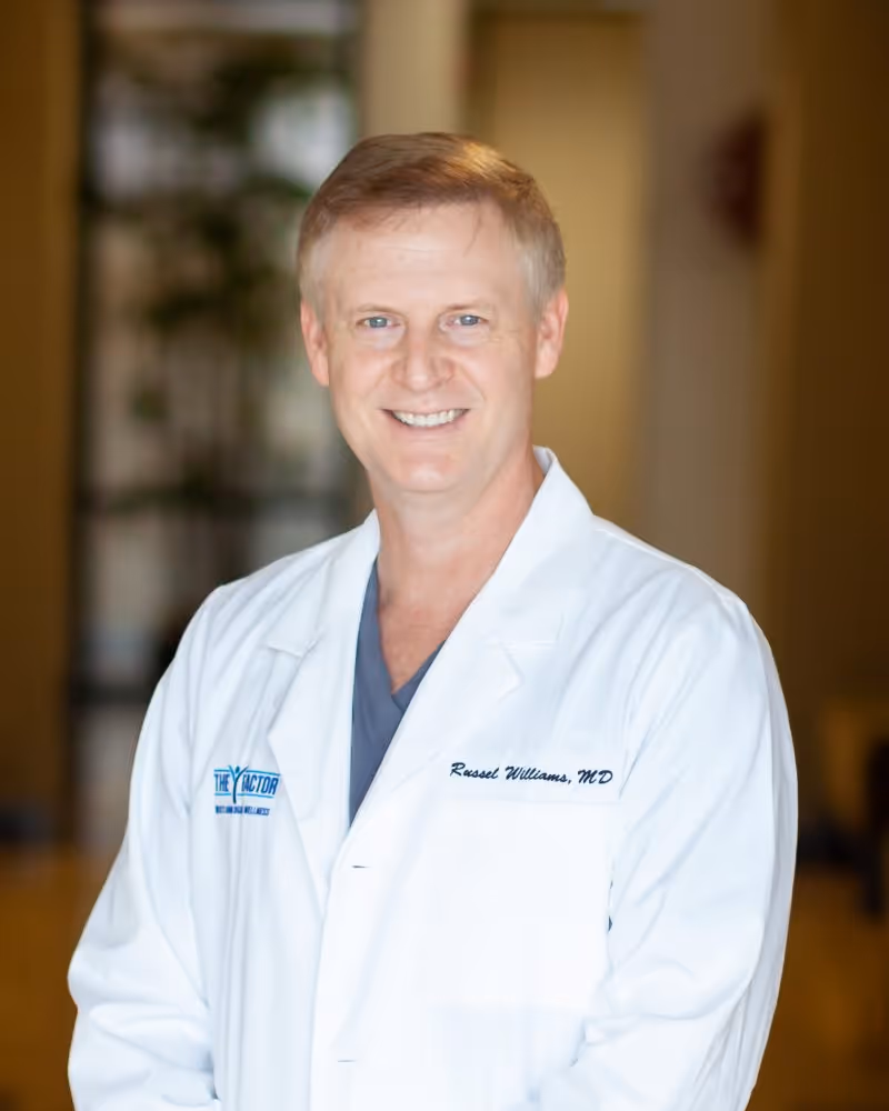 Professional portrait of a smiling male urologist in a white clinical coat.