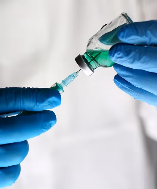 Close-up of a medical professional in blue gloves drawing medication from a vial into a syringe.
