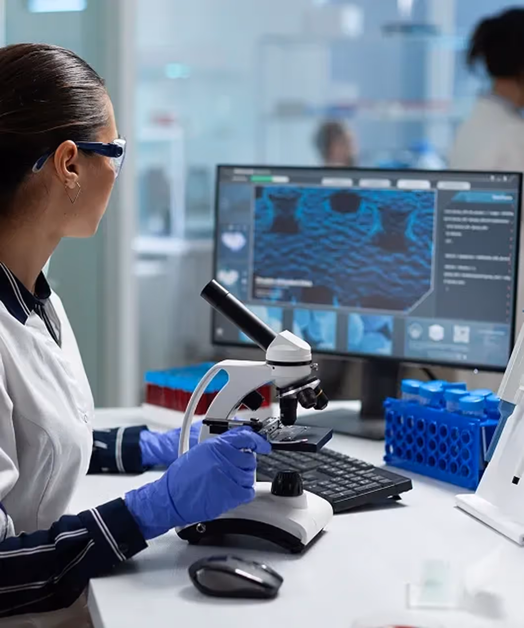 Laboratory professional in a white coat working at a microscope in a diagnostic setting.