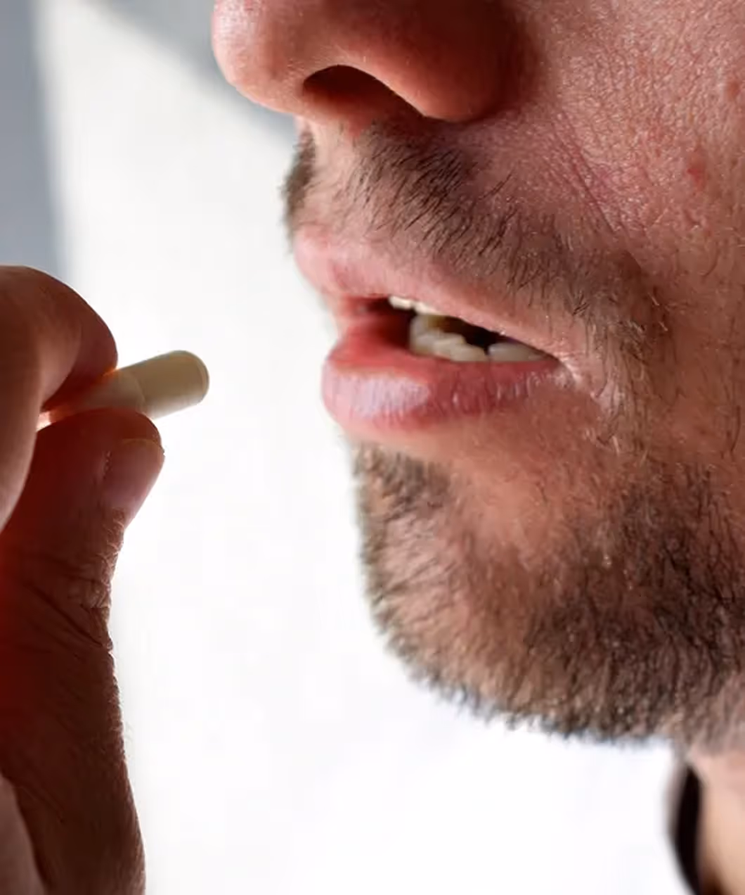 Close-up of a man placing a small white pill in his mouth for medical treatment.