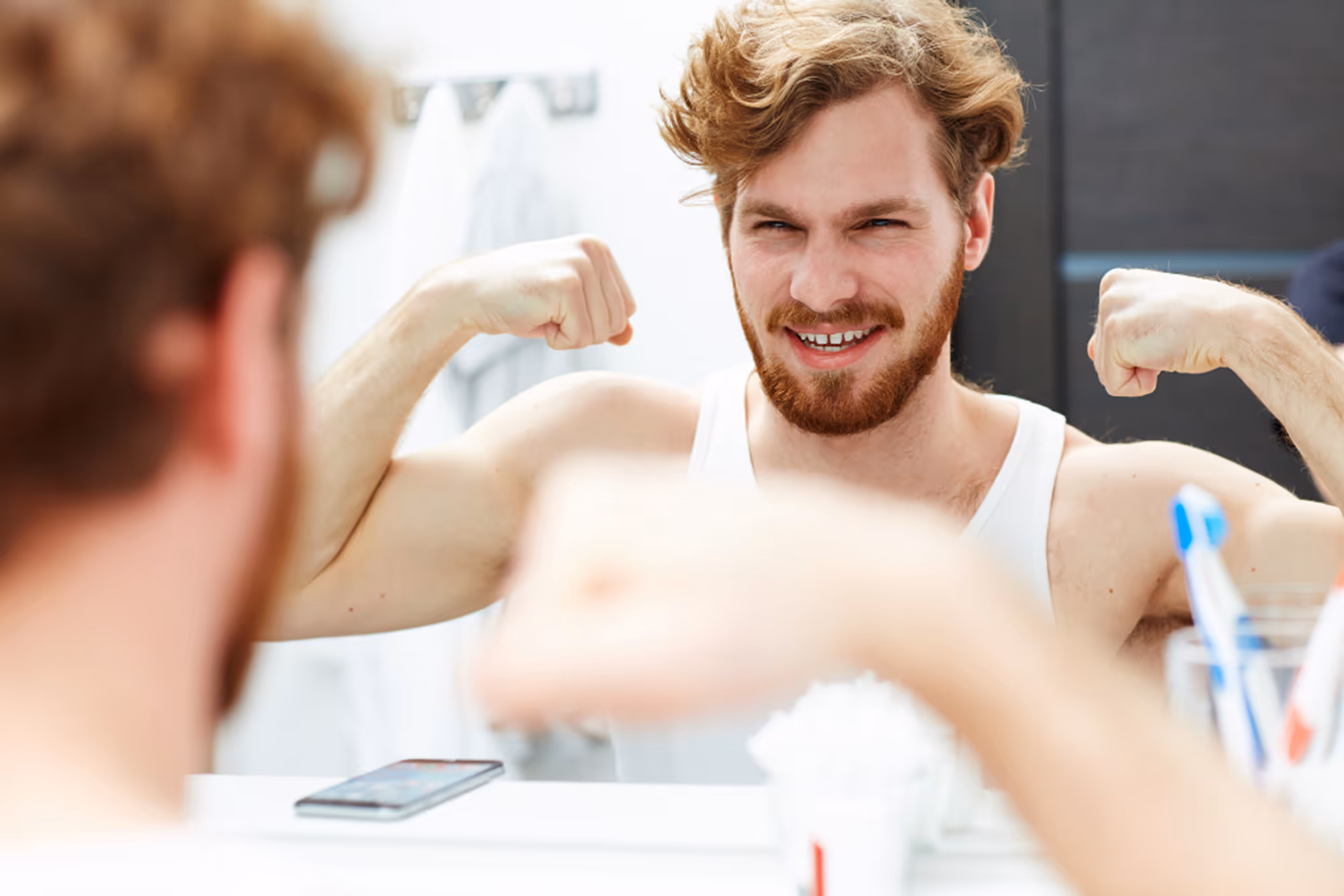 Man looking in a mirror and flexing his muscles representing physical fitness and health optimization.