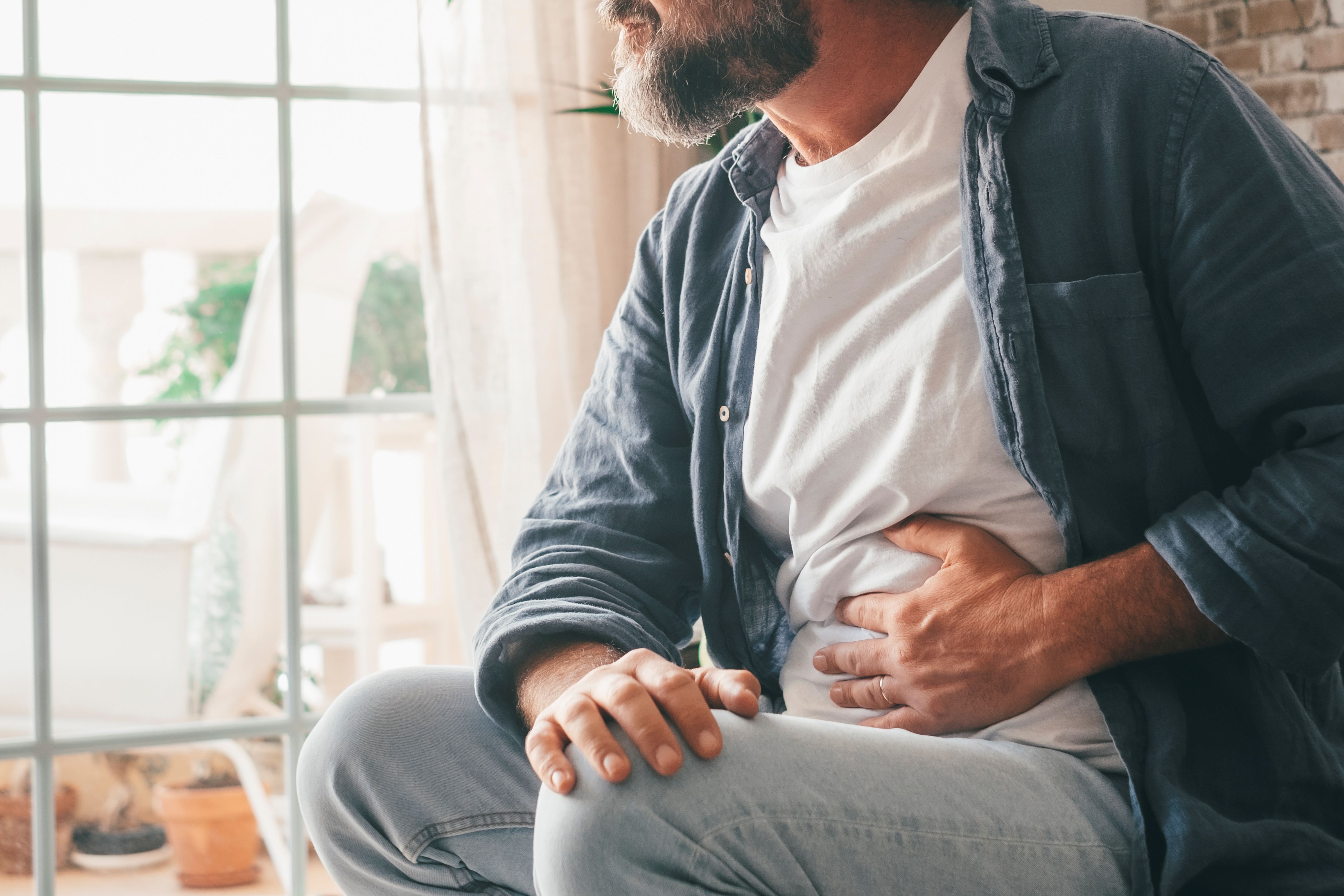 Male sitting by the window with his hand on his stomach 