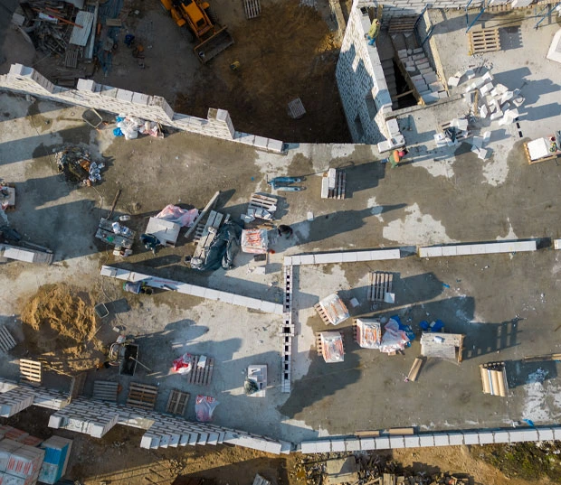 Vue aérienne d'un chantier de construction avec des murs en blocs de béton partiellement montés et des matériaux de construction éparpillés au sol.