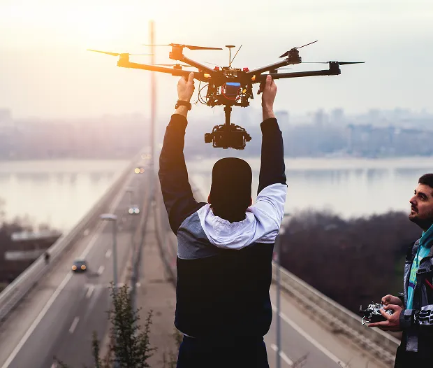 Personne tenant un drone au-dessus de la tête sur un pont avec une autre personne tenant une télécommande.
