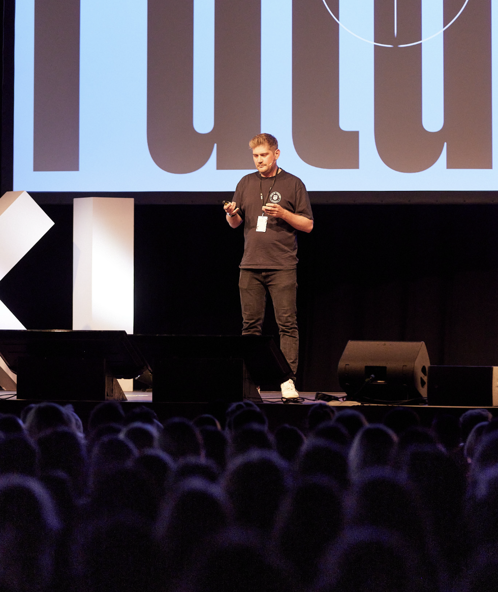 Ein Mann hält eine Präsentation auf der Bühne vor einem Publikum in einem Konferenzsaal.