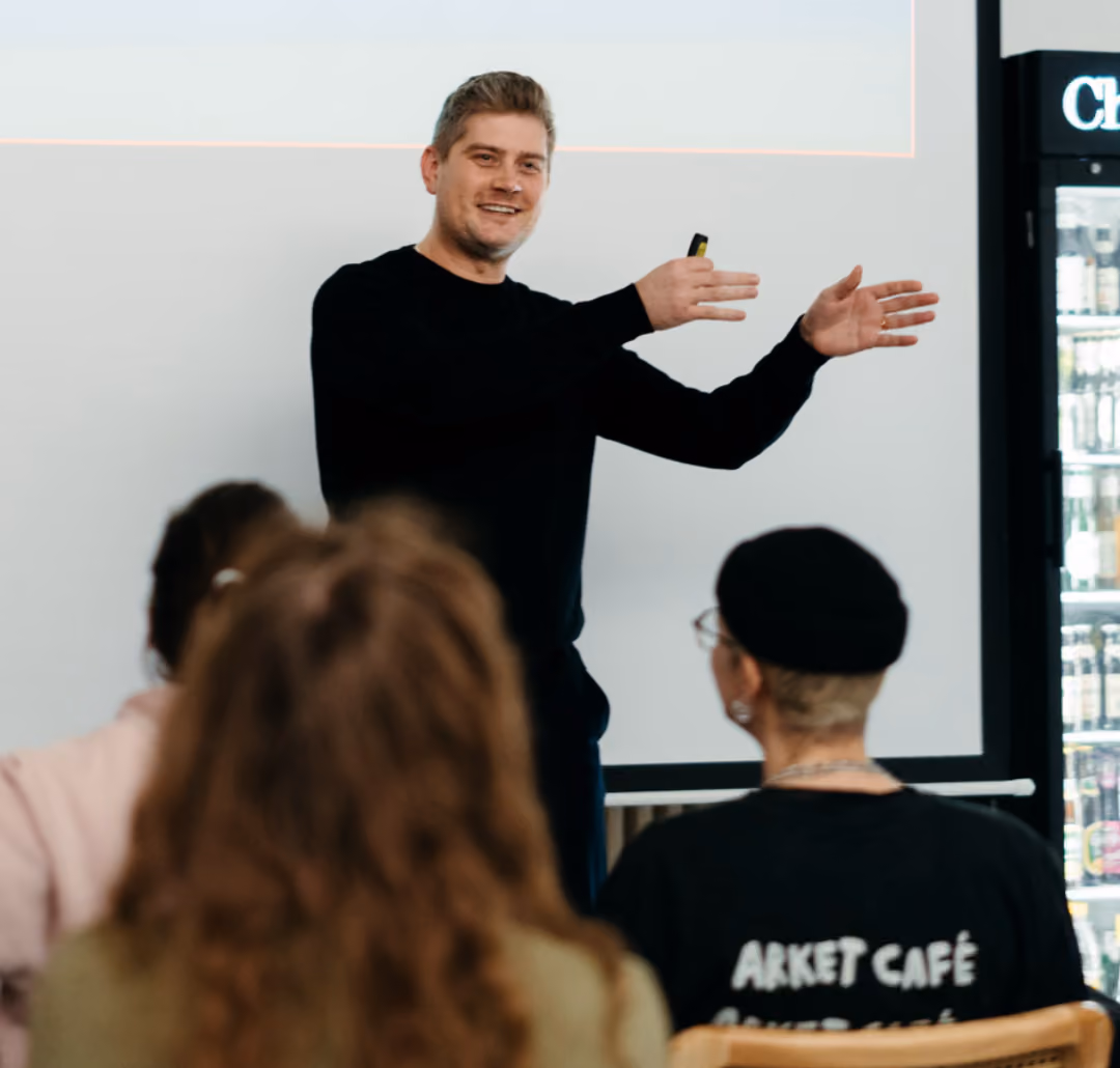 Ein Mann in schwarzem Pullover hält eine Präsentation vor einer Gruppe und gestikuliert mit den Händen.