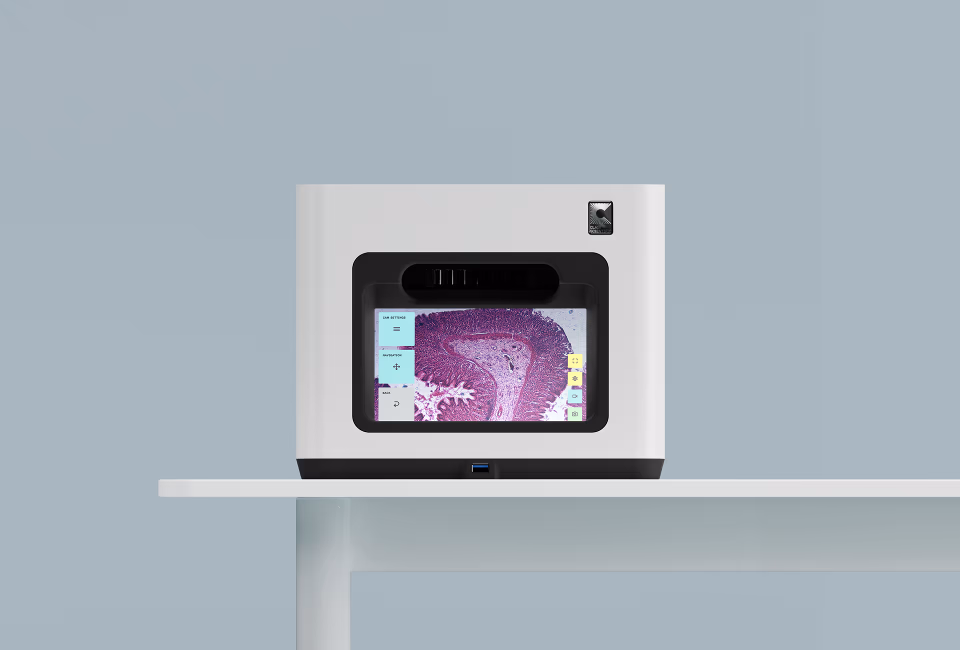 Compact lab device displaying a magnified purple tissue sample on its screen, placed on a white table against a gray background.