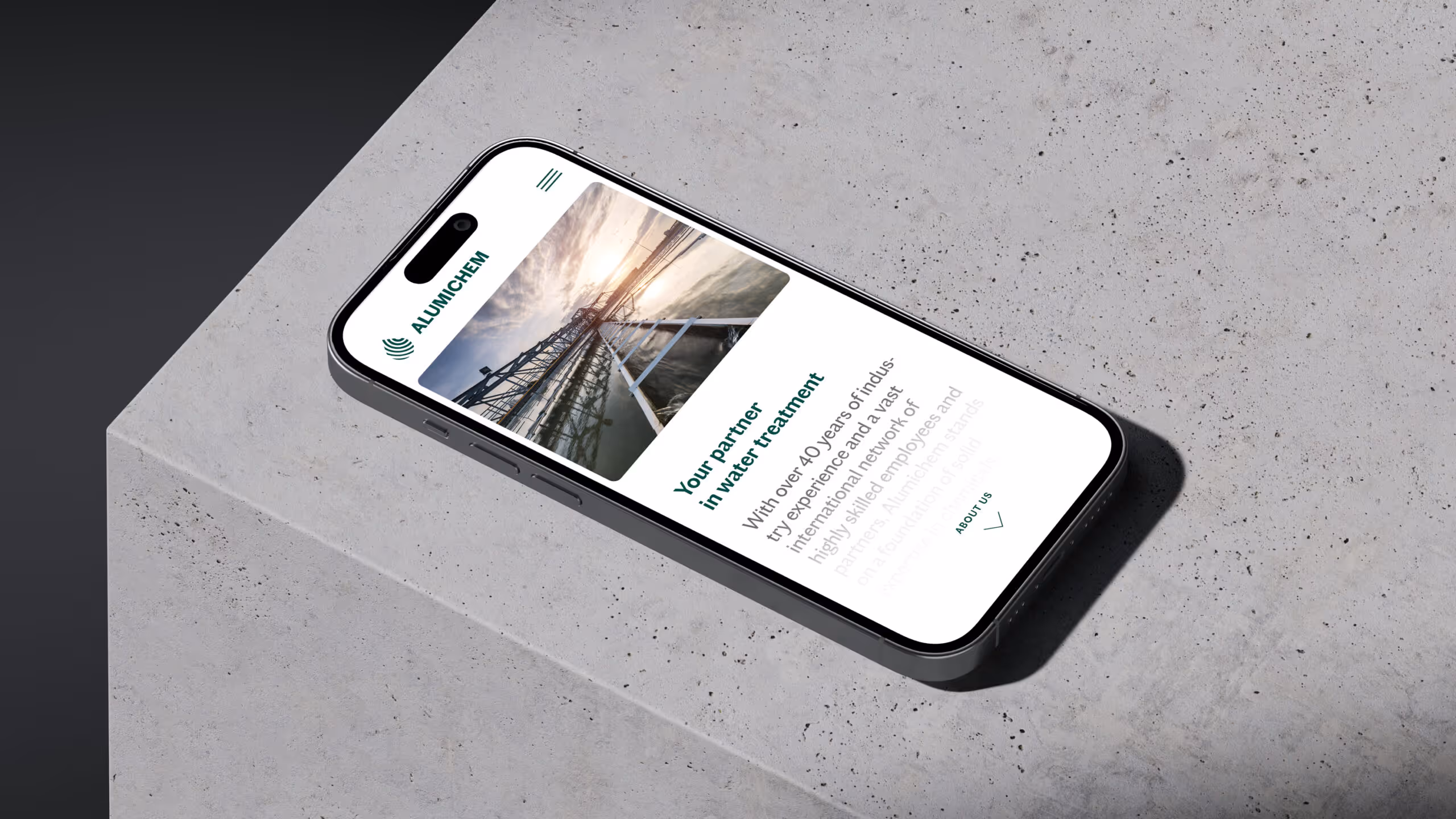 Smartphone displaying Alumichem website homepage with water treatment theme, lying on textured concrete surface.