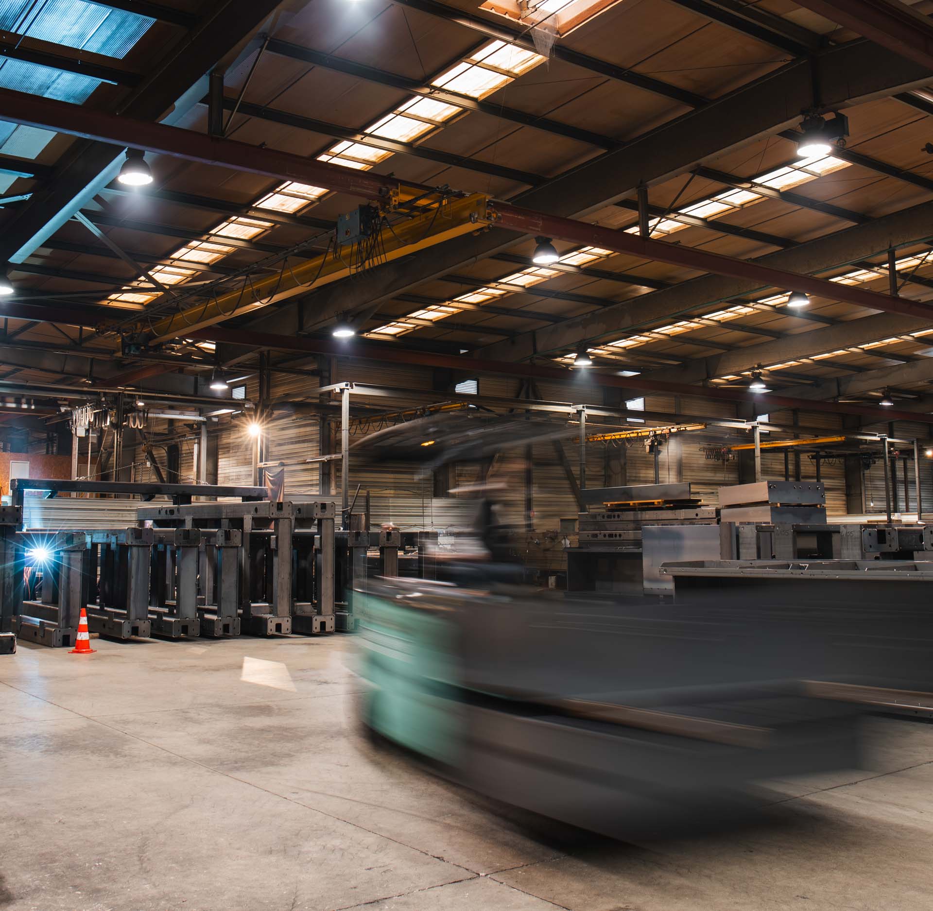 Entrepôt industriel avec un chariot de manutention en mouvement et des structures métalliques empilées.