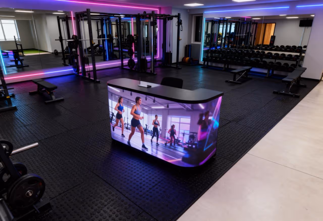 Salle de sport moderne avec un bureau lumineux affichant une image de femmes courant, entouré de poids, bancs de musculation, et équipements de fitness.