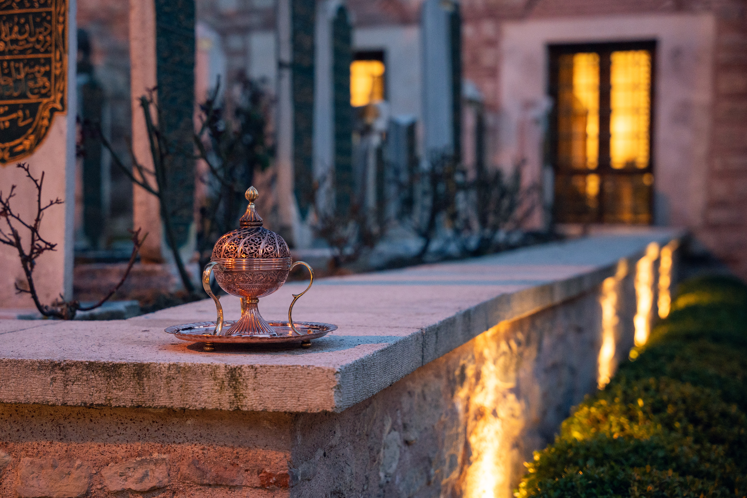 Ornate metal incense burner on a stone ledge with decorative plaques and warm lighting in the background.