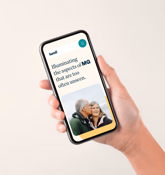 Hand holding a smartphone displaying a webpage with text about illuminating the aspects of MG and a photo of an older man kissing a woman on the cheek.