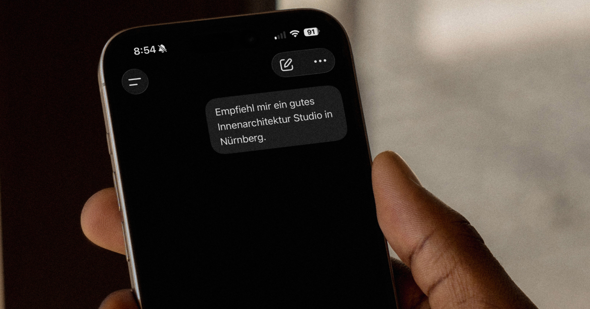 Hand hält ein Smartphone mit ChatGPT, im Chat die Frage nach einem Innenarchitektur-Studio in Nürnberg