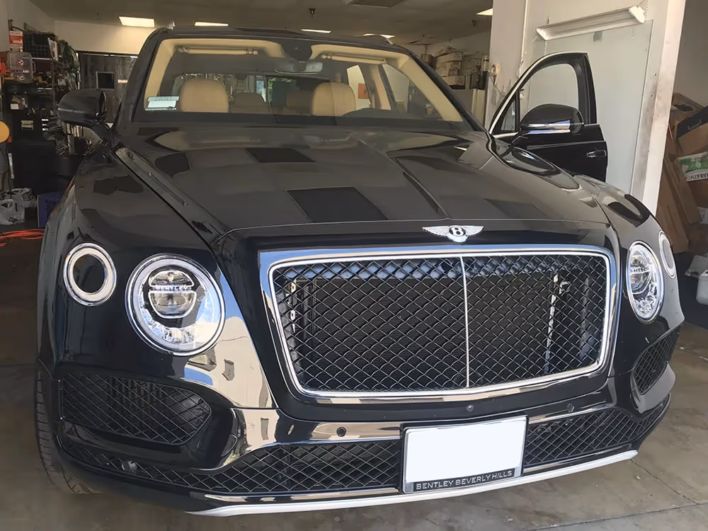 Front view of a black Bentley Bentayga luxury SUV showing the signature matrix grille, quad headlights, and tan interior.