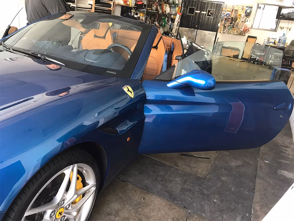 Blue Ferrari California convertible with tan leather interior and door open, parked in a showroom.
