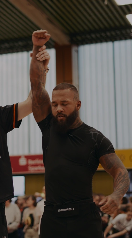 Kampfsportler mit geschlossenen Augen, dessen Hand von einem Unparteiischen als Sieger hochgehoben wird.