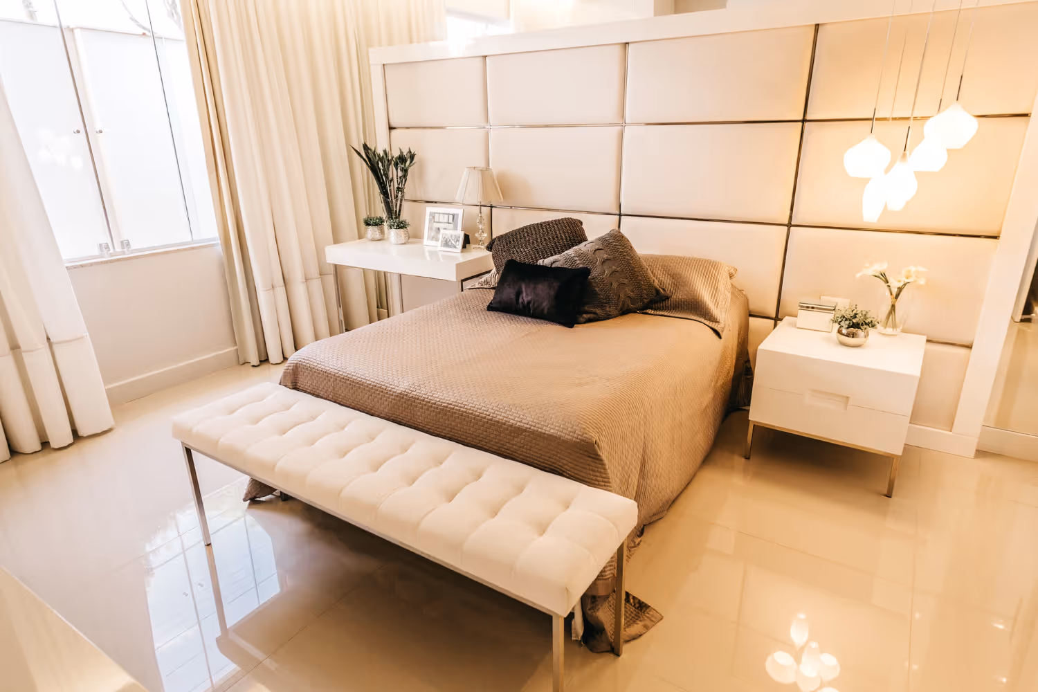 Modern bedroom with beige bedspread, tufted bench, floating nightstand with plants, and hanging pendant lights.