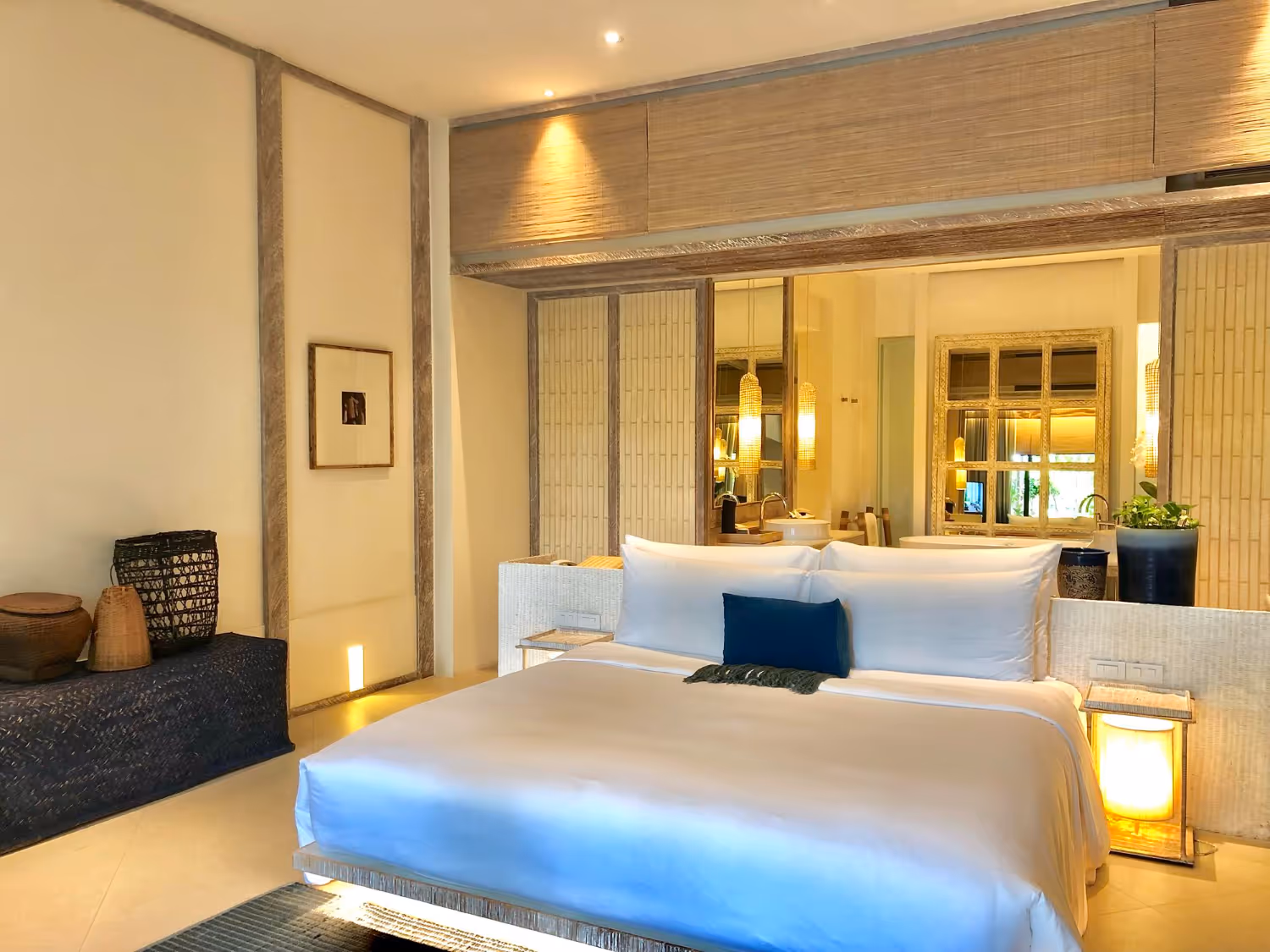 Bright and modern bedroom with a large white bed, navy blue pillow, wooden decor, and warm lighting.