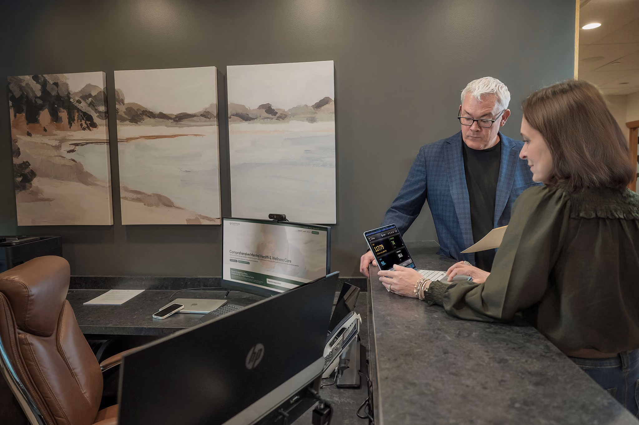 Two people at a counter looking at a tablet showing health data and heart rate metrics.