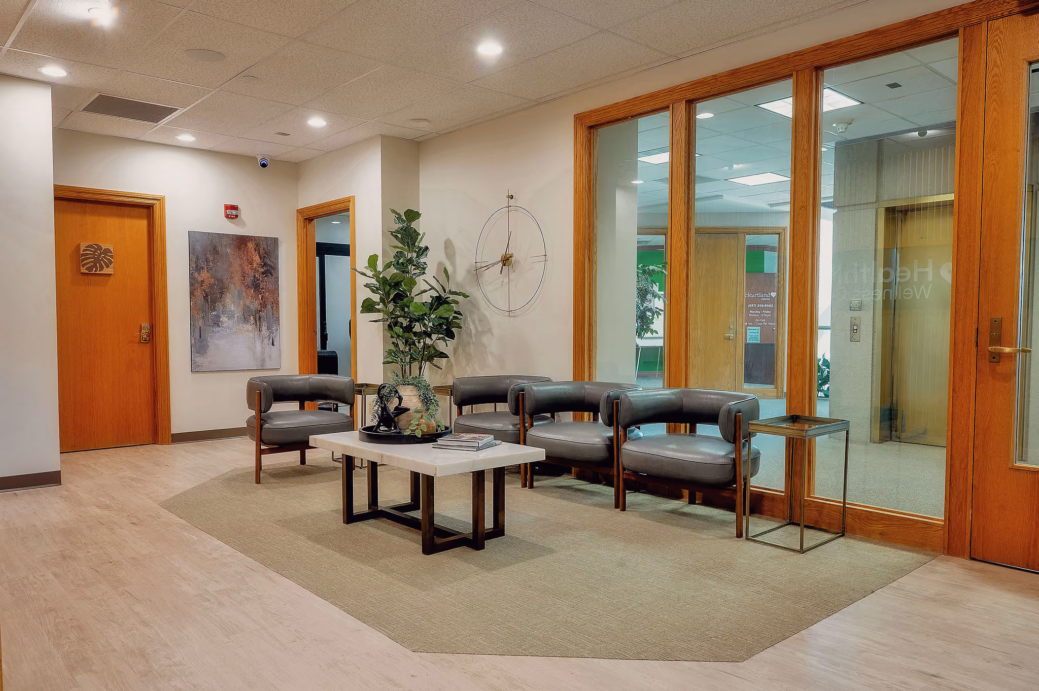 Waiting area with four dark chairs, a coffee table with books and plant, and wooden doors.