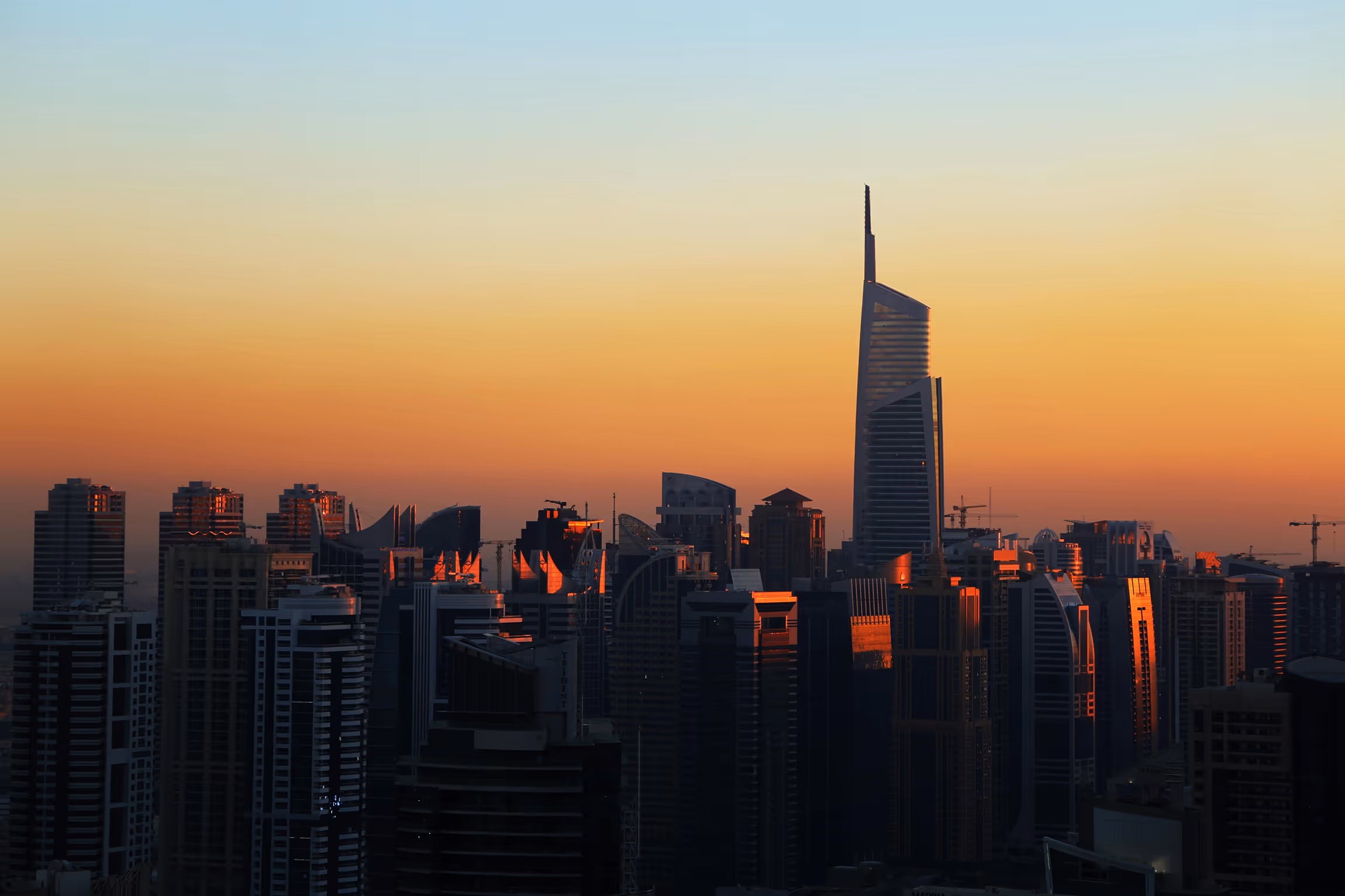 City skyline at sunset with tall modern skyscrapers reflecting orange sunlight.