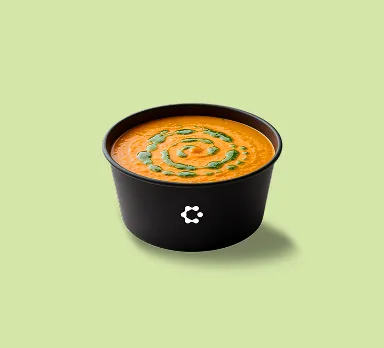 A black bowl filled with tomato soup garnished with green swirl pattern, featuring a white Circus icon on the front.