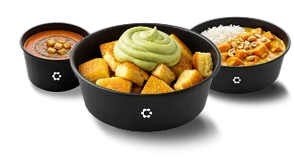 A presentation of three black bowls featuring different meals: the front bowl contains crispy golden croutons topped with a swirl of green sauce, while the back bowls display tomato soup with croutons and a curry dish with rice and peanuts, all against a dark background.