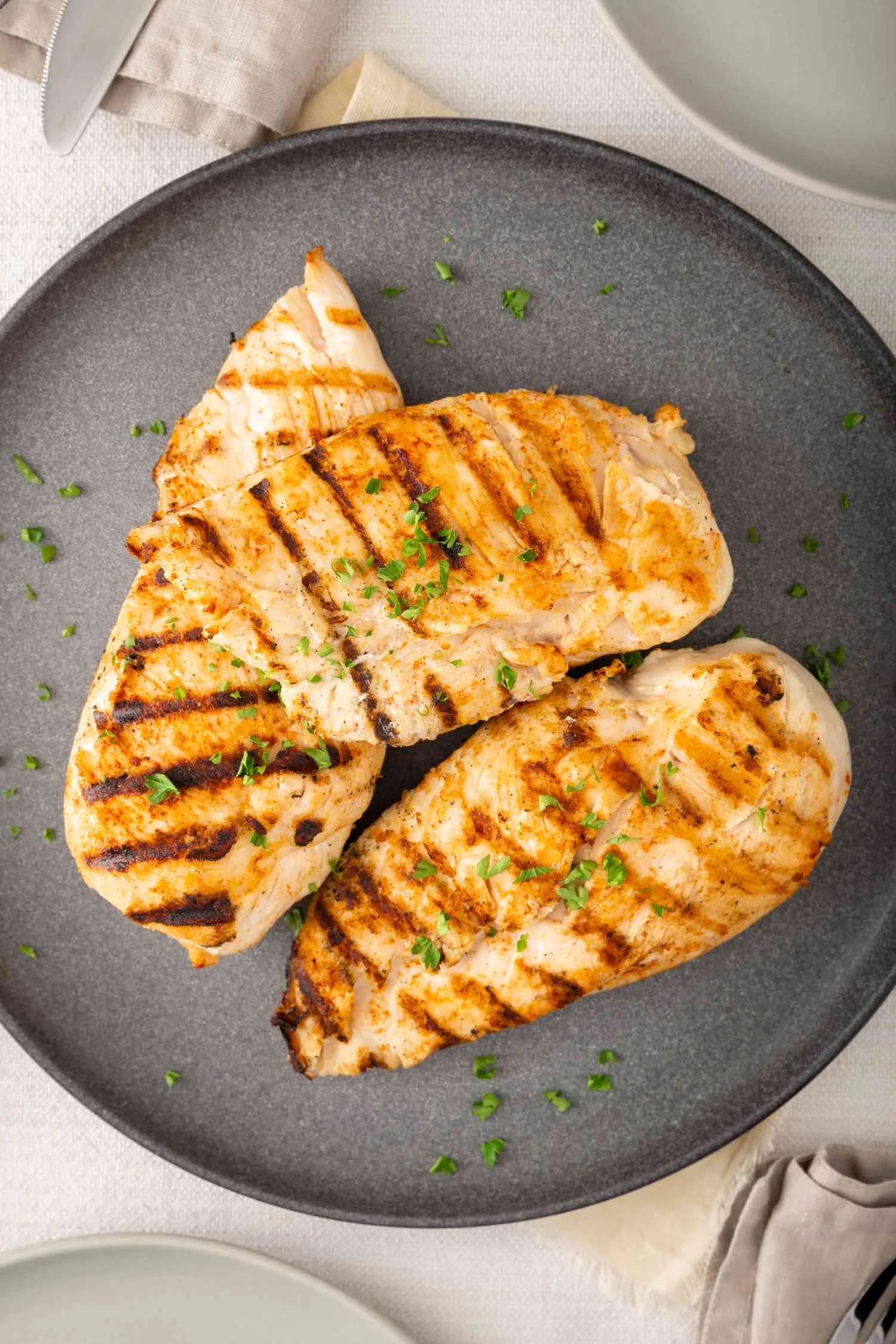 Two grilled chicken breasts garnished with chopped herbs on a gray ceramic plate.