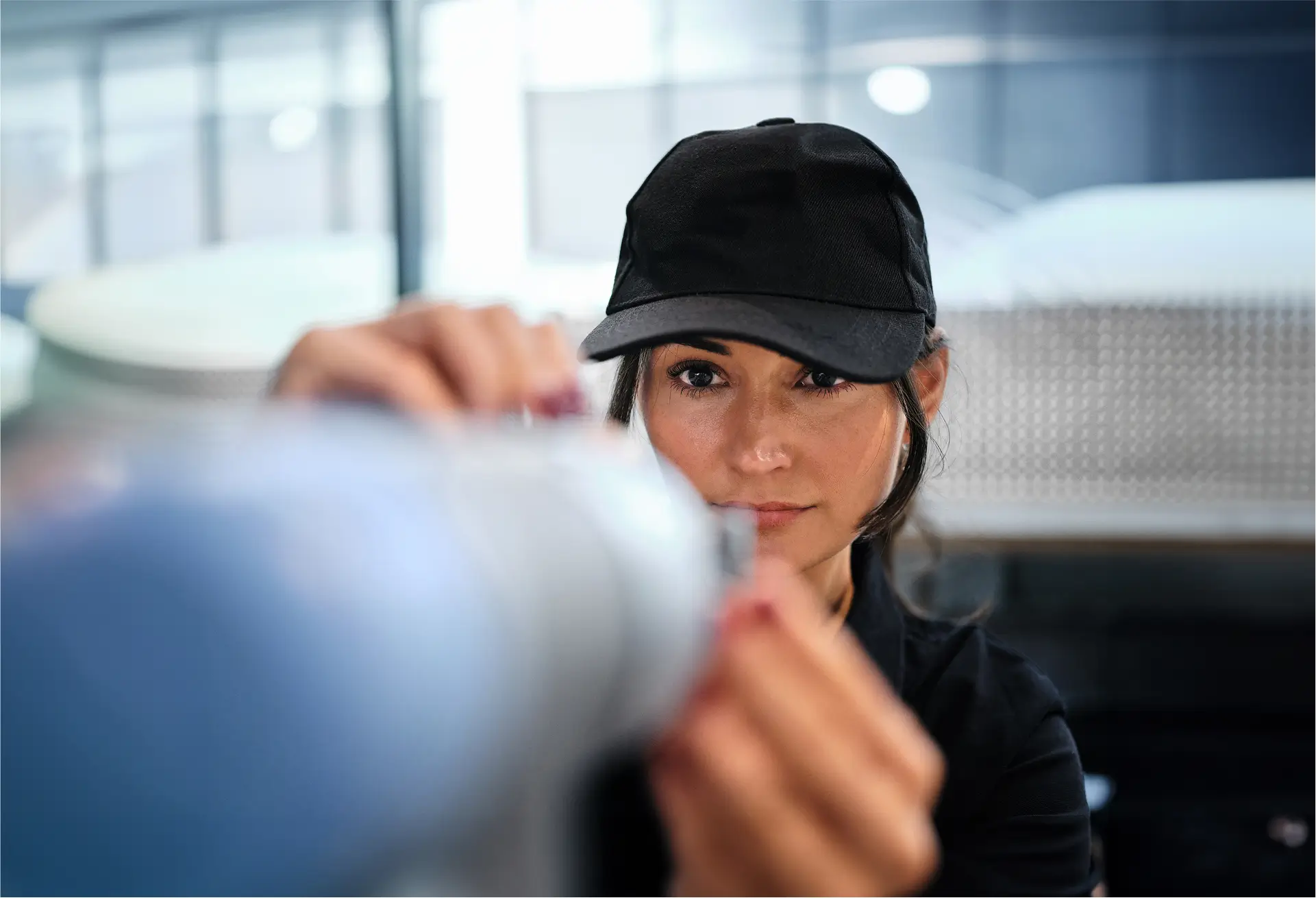 Woman wearing a black cap closely examining a fabric sample in a modern workspace.