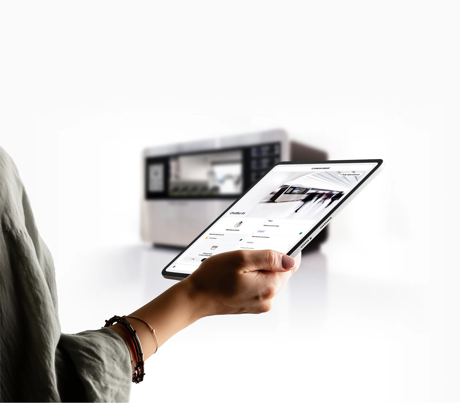 Person holding a tablet with the CIRCUS OS dashboard interface on screen, remotely monitoring a CA-I Series 4 robotic kitchen unit in the background.
