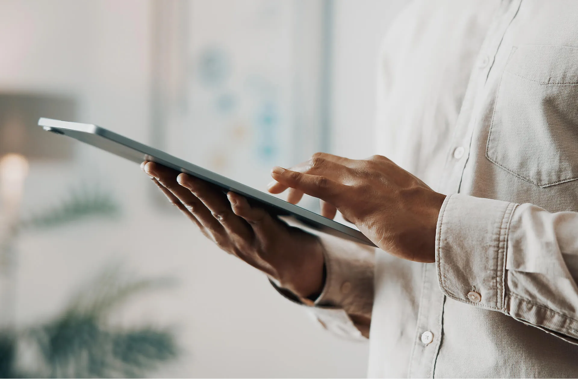 Close-up of a person in a light-colored shirt using a digital tablet indoors.