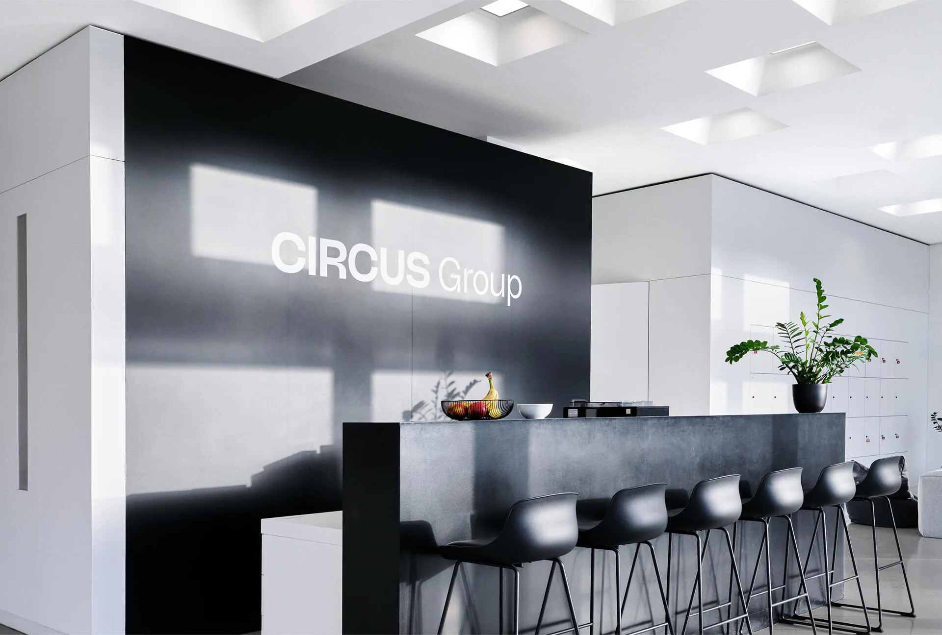 Modern reception area of the Circus Group office featuring a sleek black counter, bar stools, minimalist décor, and bold white company branding on a black wall.
