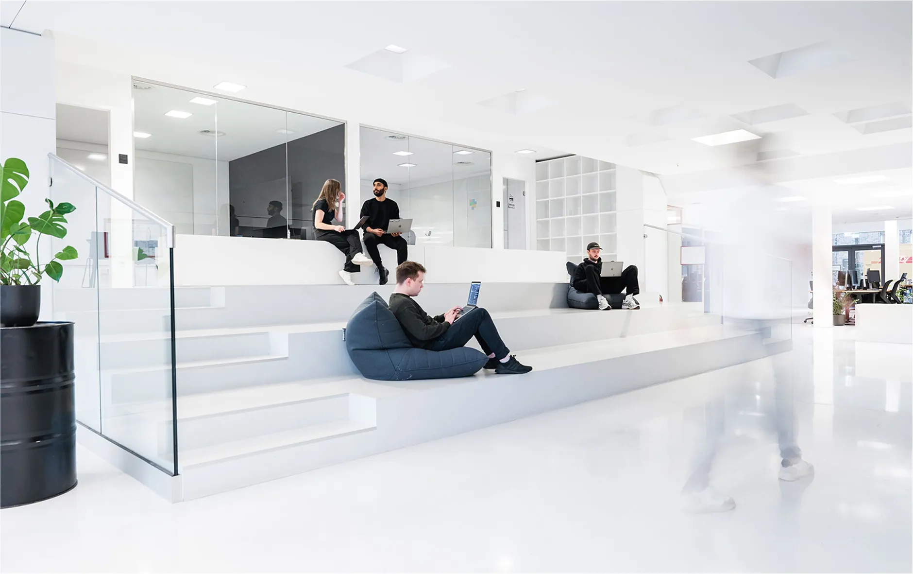 Modern, bright white office space at the Circus Group Hamburg Office, with employees working on laptops while seated on tiered steps and bean bags.