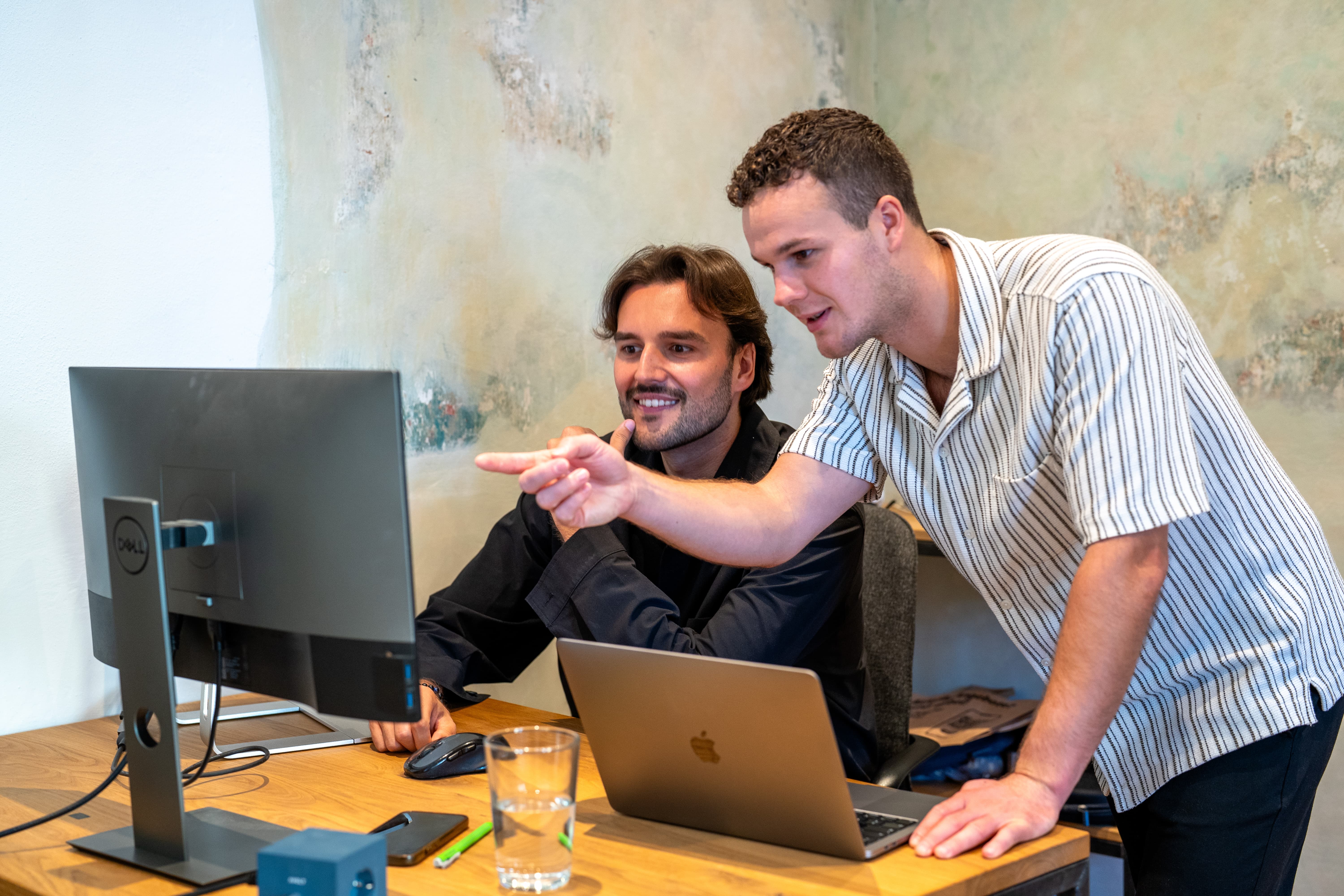 Zwei Männer arbeiten zusammen an einem Computer, einer zeigt auf den Bildschirm.