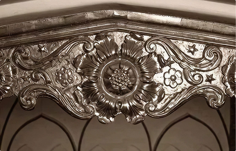 Intricate metallic floral and star patterns carved on an ornamental arch or frame.
