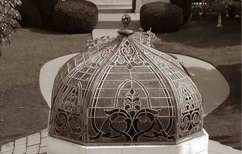 Decorative ornate metal cage structure with intricate floral and geometric patterns on a tiled base.