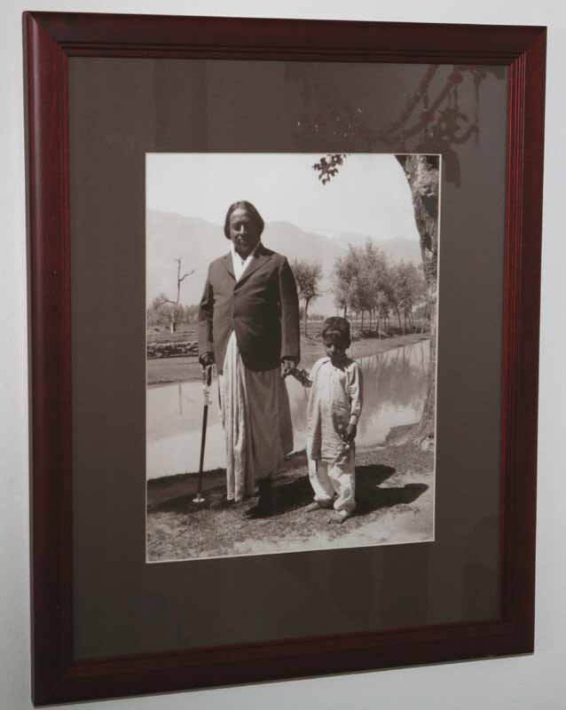 Framed black-and-white photo of Paramahansa Yogananda holding a child's hand by a pond outdoors.