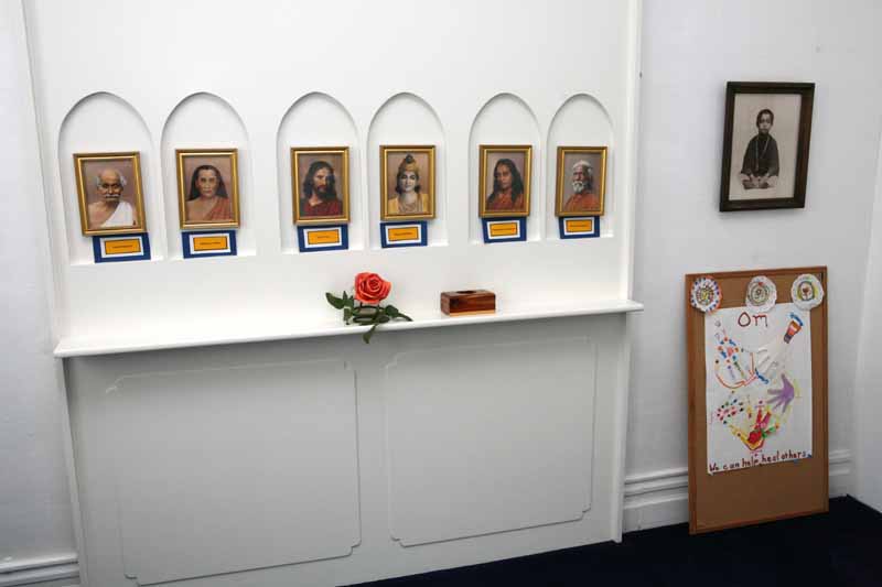 Wall with six framed portraits in arched niches, a red rose on a shelf, and a framed photo and artwork on the side.