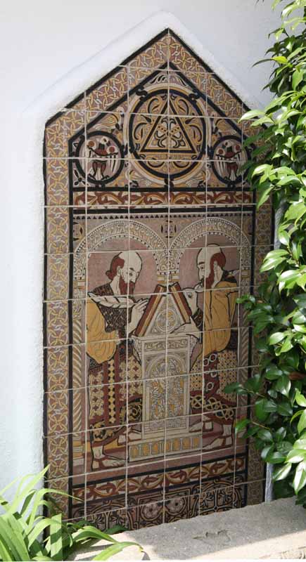 Decorative tile artwork depicting two figures with scrolls facing each other in an ornate arched frame.