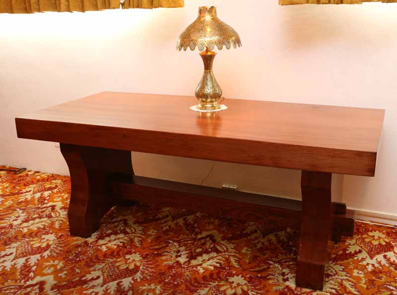 Polished wooden table with ornate golden lamp on a patterned orange carpet under yellow curtains.