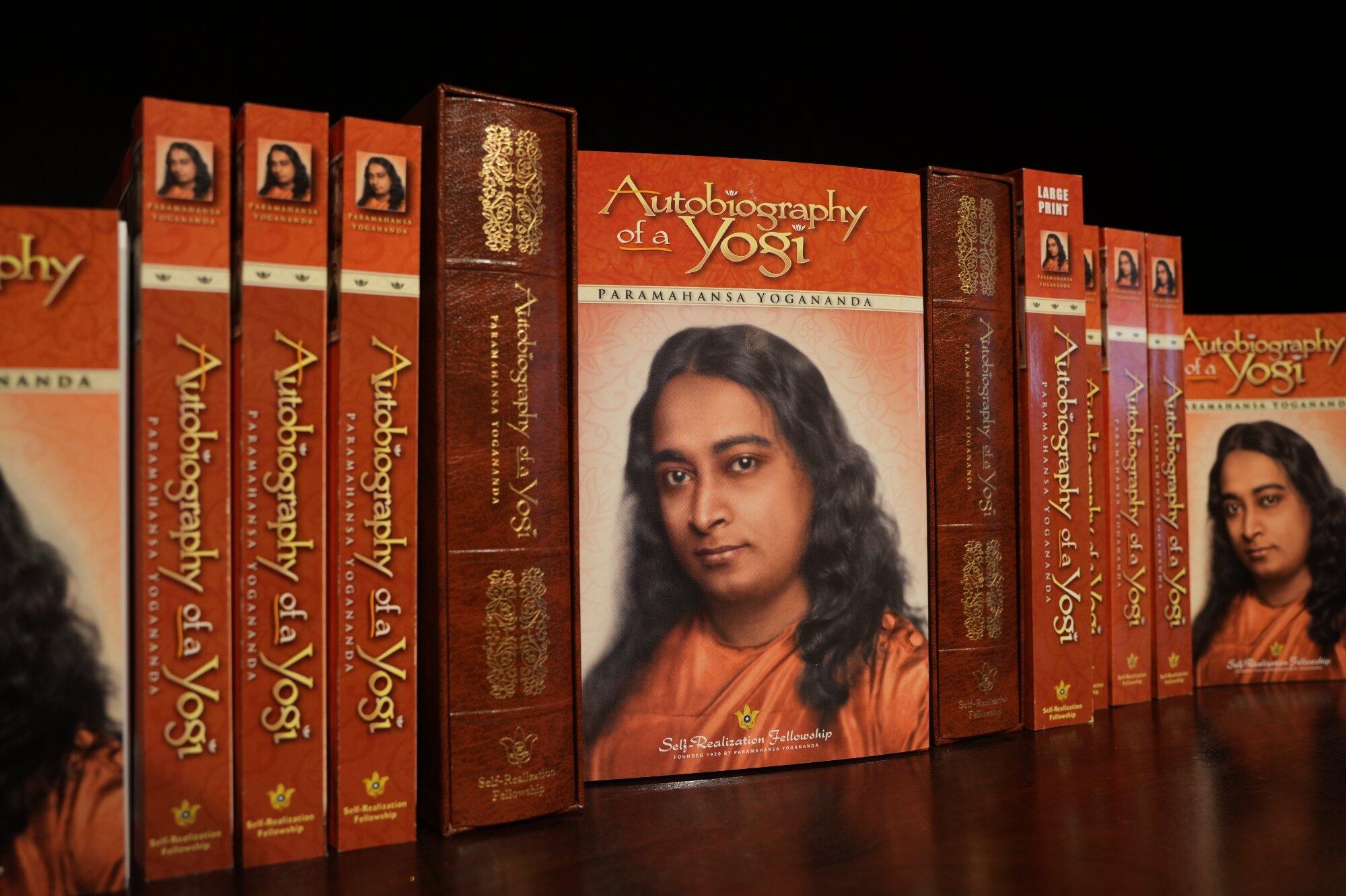 Multiple copies of the book 'Autobiography of a Yogi' by Paramahansa Yogananda on a wooden shelf.