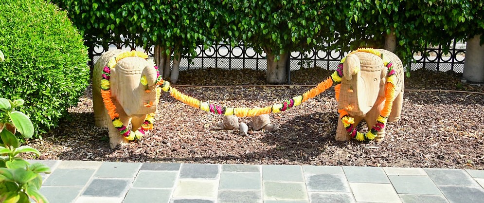 Two stone bull statues adorned with colorful flower garlands connected by a garland in a garden bed.