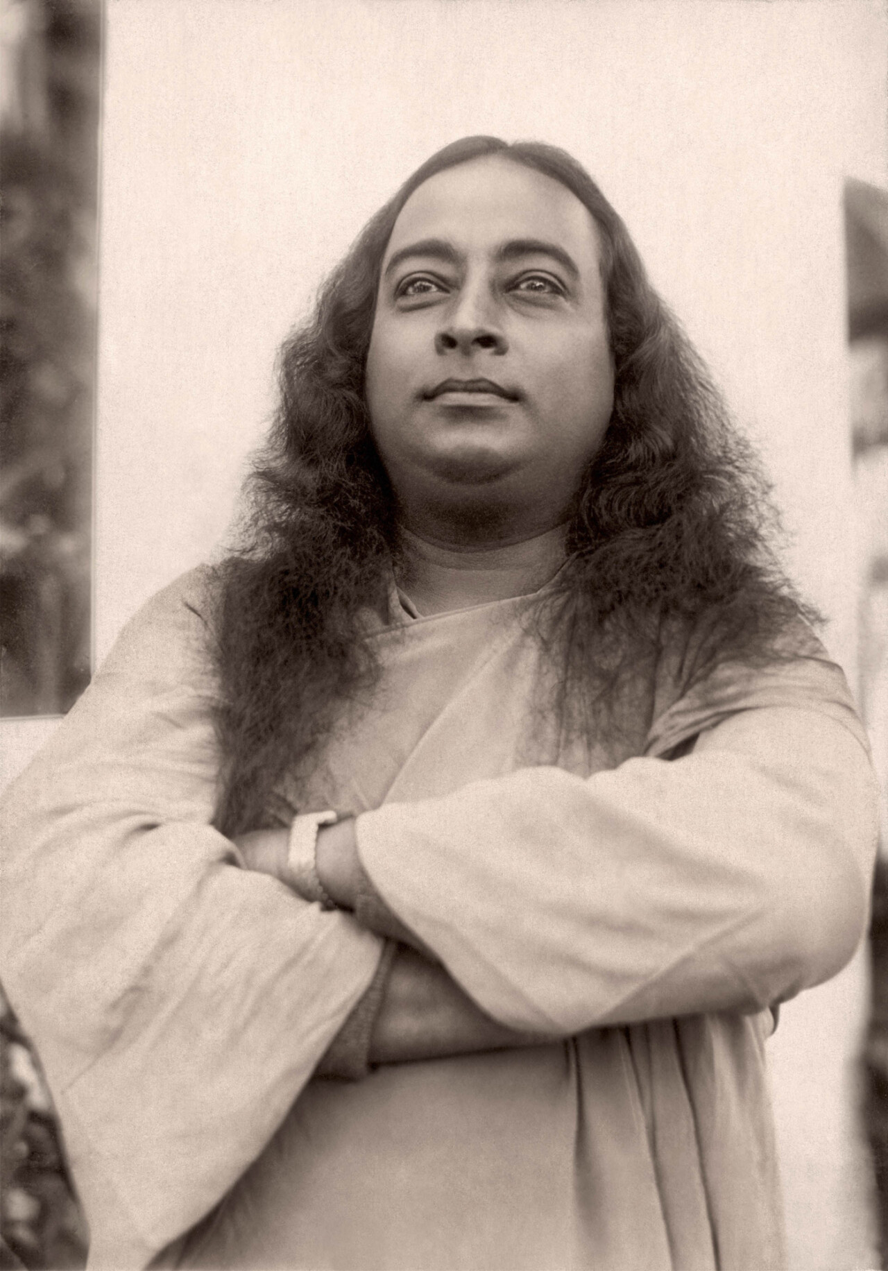 Portrait of Paramahansa Yogananda wearing traditional robes, arms crossed and gazing upward.