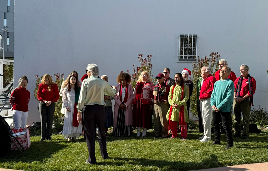 Members of the Hollywood Temple Singers standing outdoors on grass, singing with a man directing them.