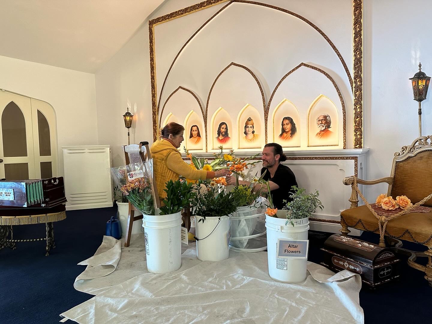 Two people arranging flowers in buckets labeled Altar Flowers inside the temple at SRF Hollywood Temple