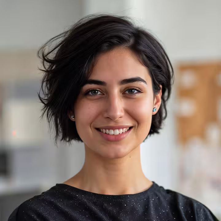 Smiling person with side-swept short hair in a bright indoor setting.