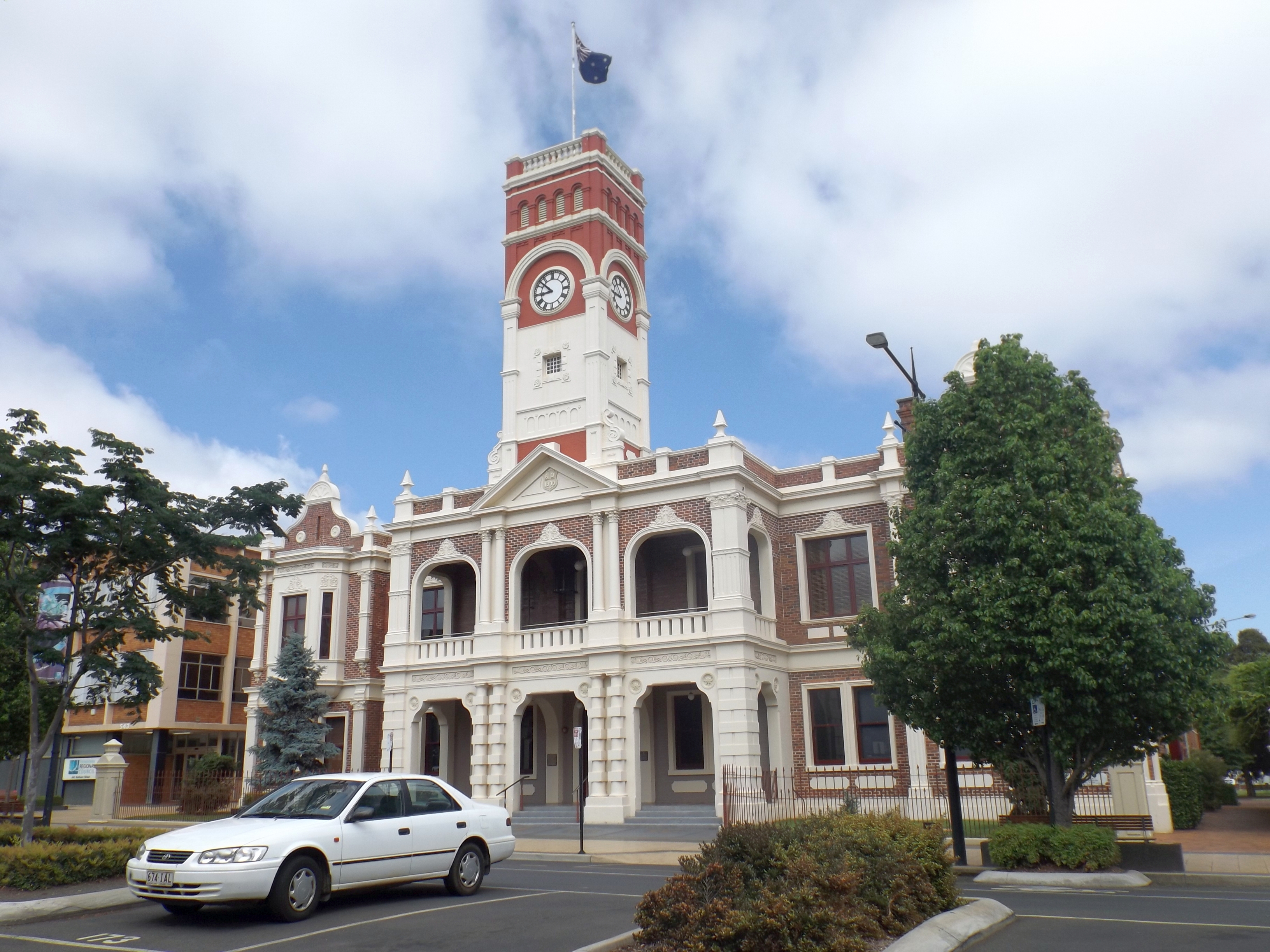 Historic civic building with clock tower in Toowoomba, with a car parked in front and trees lining the street.