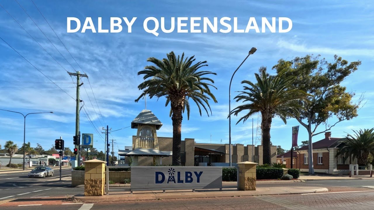 Street scene in Dalby featuring palm trees and a welcome sign under a blue sky.