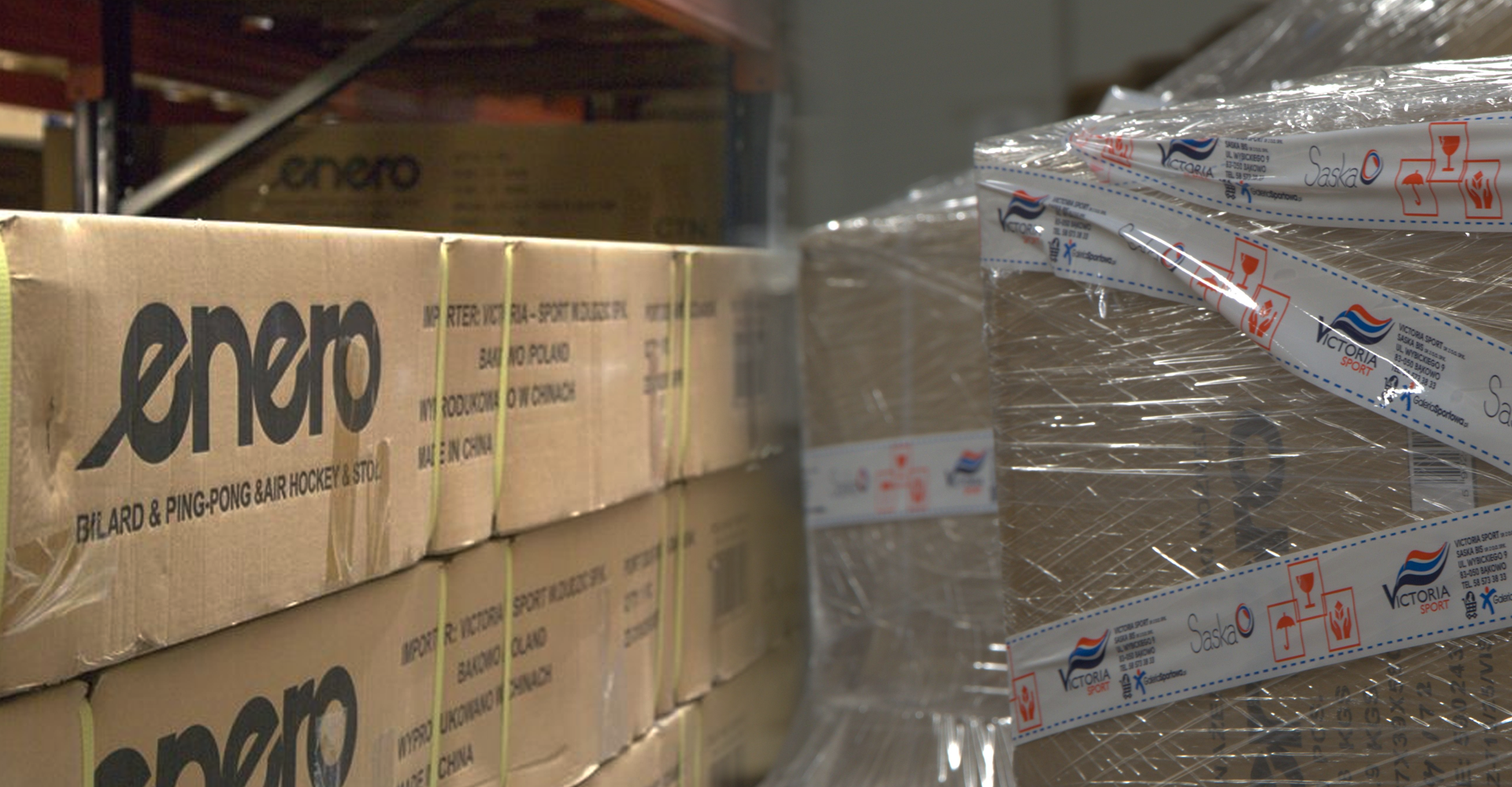 Stosy kartonowych pudeł z logo enero i owinięte taśmą transportową z napisem Victoria Sport w magazynie.