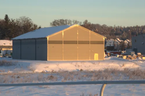 Hala magazynowa victoria sport oświetlona promieniami zachodzącego słońca na tle zaśnieżonego pola i lasu.